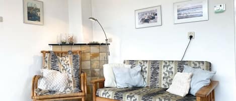Een kamer met een houten bank en stoel, een open haard en ingelijste foto’s aan de muur.