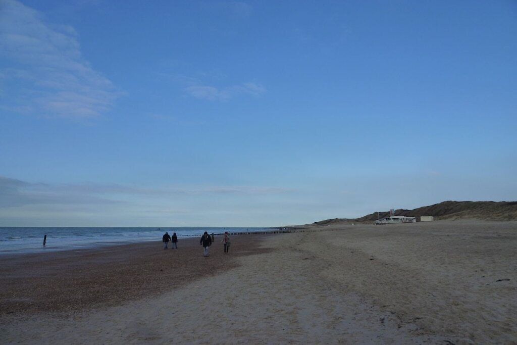 A wide sandy beach with a clear sky and a few people walking.