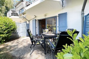 An outdoor patio with a table and chairs, a covered area, and a building with blue shutters. - Holiday apartment with 1 bedroom (Dierhagen)