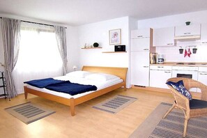 A bedroom with a bed, a chair, a kitchenette, and a window with curtains. - 1 Buchenheim House Rena (Reifnitz)