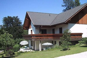A two-story building with a sloped roof, a balcony with wooden railings, and a covered outdoor seating area with umbrellas. - 1 Buchenheim House Rena (Reifnitz)
