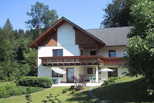 A two-story house with a balcony, a covered patio with outdoor furniture, and a well-maintained garden. - 1 Buchenheim House Rena (Reifnitz)