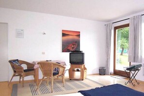 A room with a television, a dining table with chairs, a window with curtains, and a painting on the wall. - 1 Buchenheim House Rena (Reifnitz)
