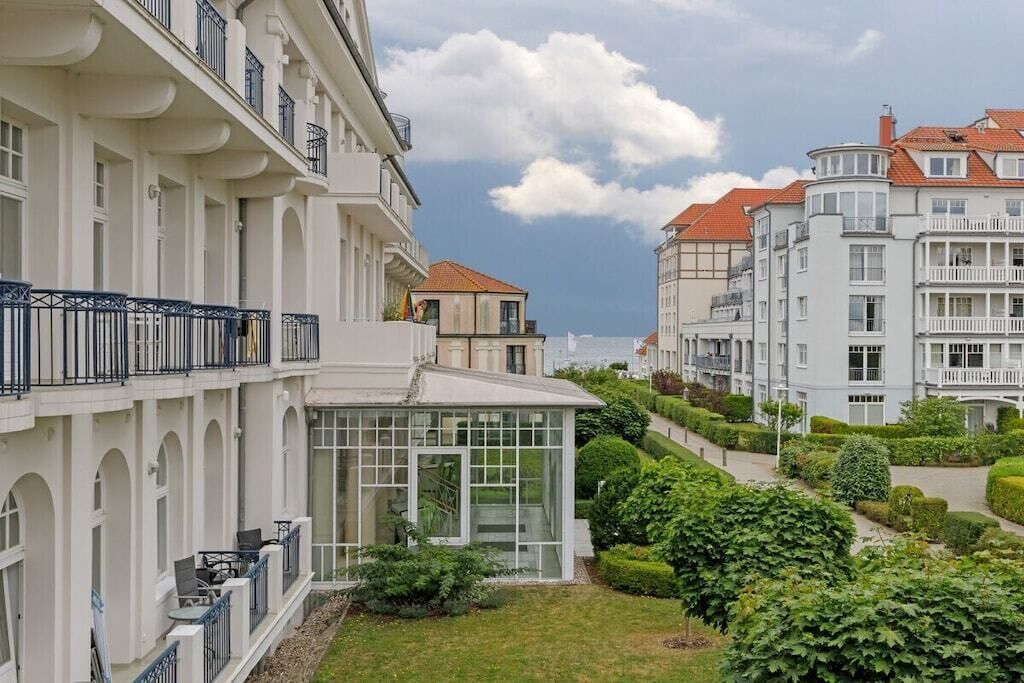 Un edificio residencial de varios pisos con balcones, un invernadero y un jardín cuidado.