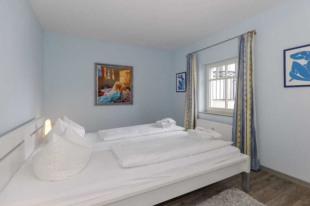 Un dormitorio con una cama, una ventana con cortinas y dos cuadros en la pared.