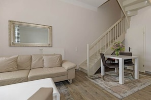 A living room with a sofa, a dining table with chairs, a staircase, and a large mirror on the wall. - Holiday apartment Haus am Park 322251 (Kühlungsborn)