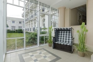 Ein Zimmer mit großen Fenstern, einer karierten Bank und Blumentöpfen.