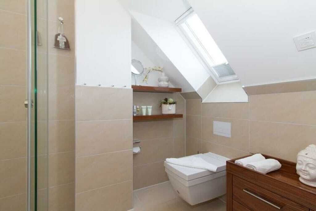 A modern bathroom with a skylight, a toilet, a vanity with a mirror, and a small shelf with toiletries.