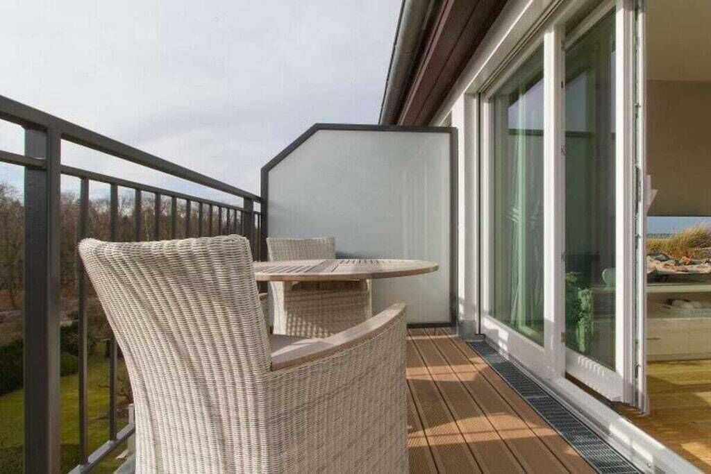 Un balcon doté de meubles en osier, d’une porte vitrée et offrant une vue sur l’extérieur.