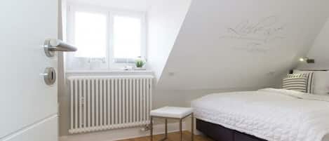 Un dormitorio con cama, radiador, ventana y puerta.