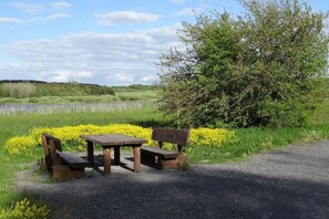 A picnic table and benches in a natural setting with a body of water and greenery in the background. - 2 Decker Elms Volcanic Eifel (Ulmen)