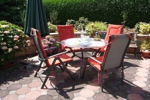 An outdoor patio with a round table and four chairs, surrounded by potted plants and a green umbrella. - 2 Decker Elms Volcanic Eifel (Ulmen)