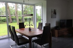 Een eetgedeelte met een houten tafel en stoelen, een televisie en uitzicht op de omgeving.