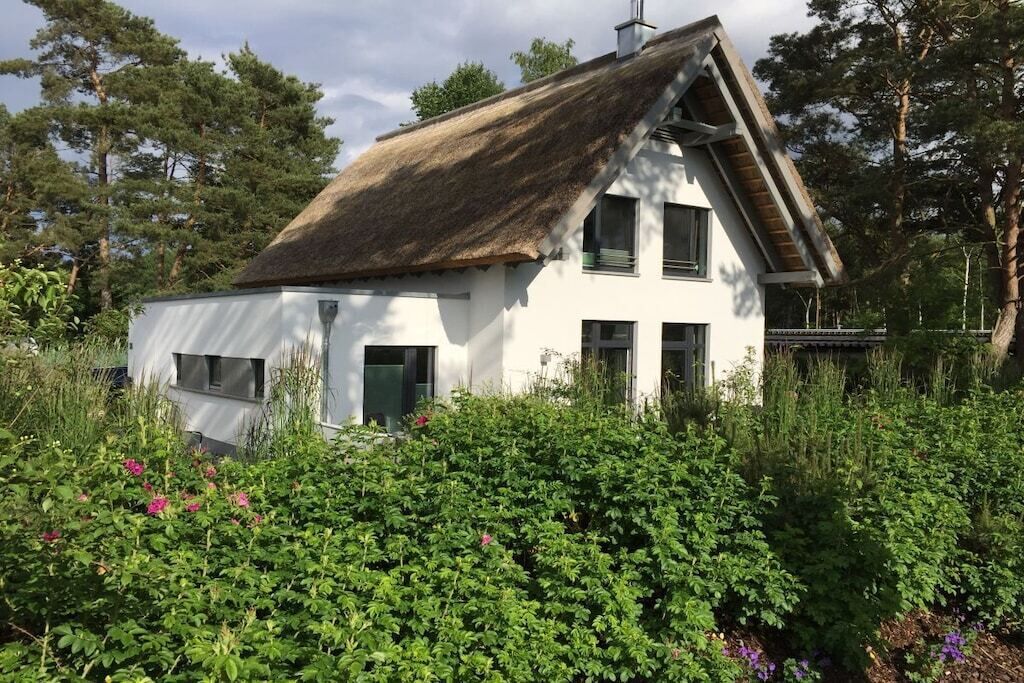 Una casa bianca con tetto di paglia circondata da vegetazione lussureggiante e piante fiorite.