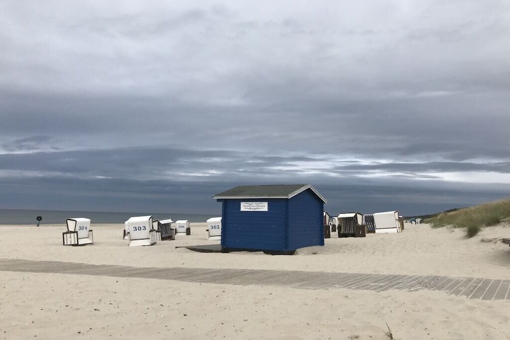 A beach with numbered beach huts and a small blue structure.