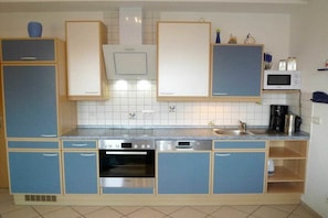 A compact kitchen with blue cabinets, a built-in oven, a microwave, and a coffee maker. - Baltic Sea view - beach only 190m (Karlshagen)