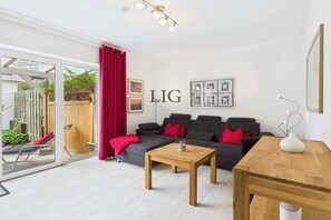 A modern living room with a grey sofa, red cushions, a wooden coffee table, and a glass door leading to an outdoor area. - Holiday apartment Strandhaus 7 (Langeoog)