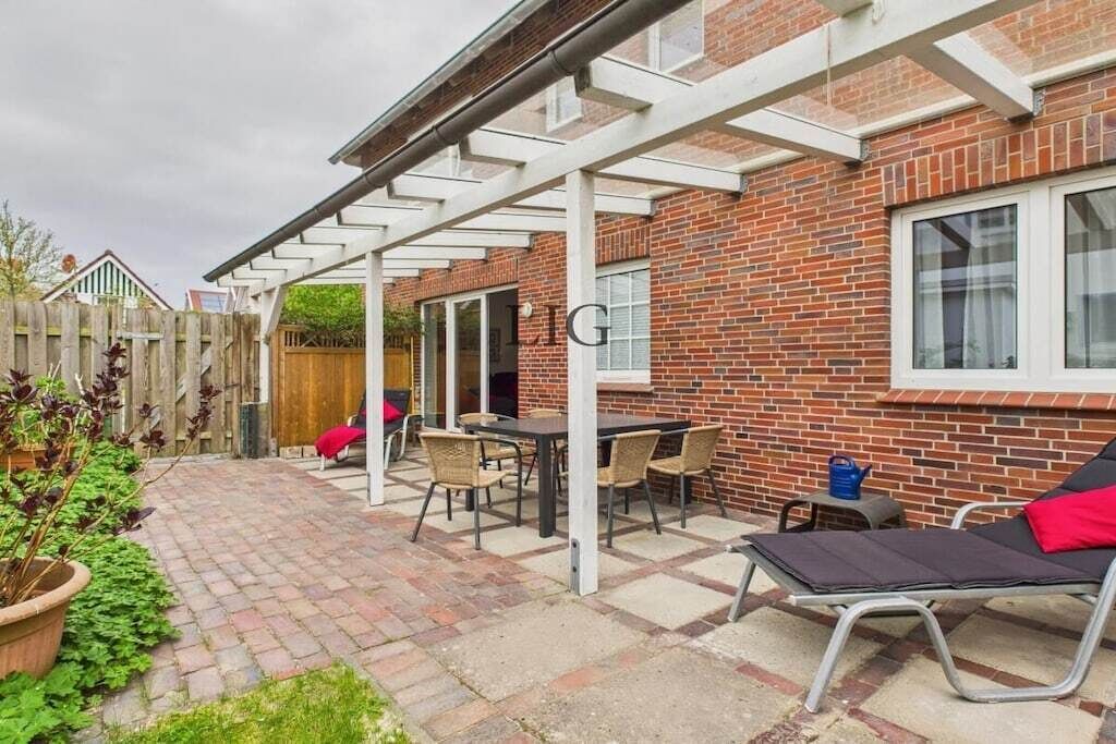 Eine Terrasse mit Tisch und Stühlen, einer Liege und einem Backsteinhaus mit Fenster.
