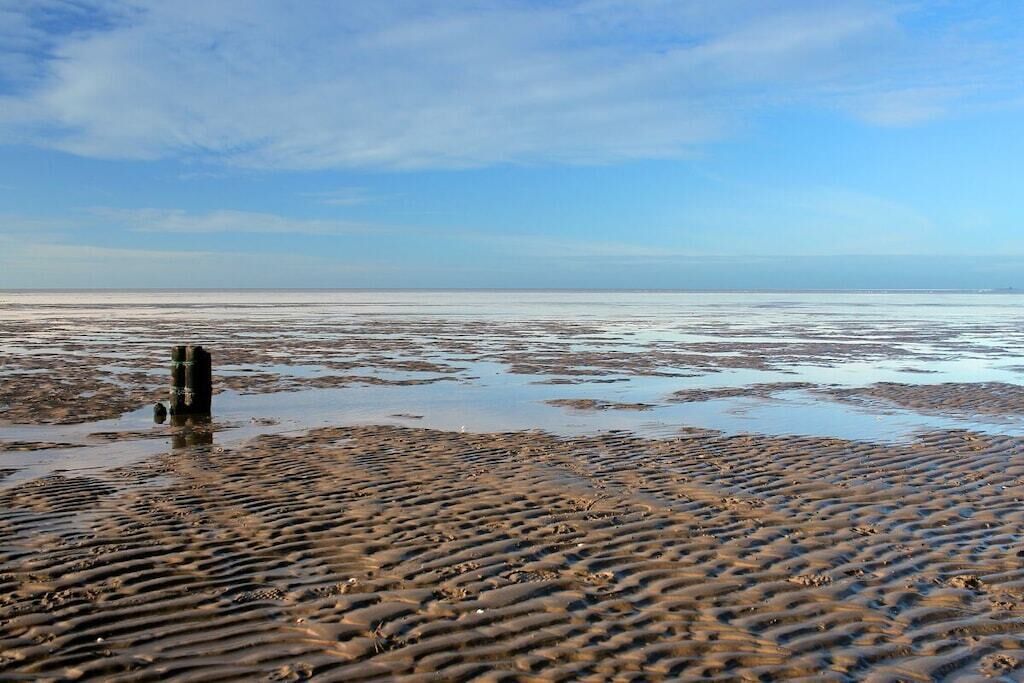 A beach with a wooden post in the foreground and a calm sea in the background.