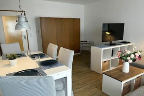 Un soggiorno moderno con zona pranzo, TV su un supporto e un armadio in legno.