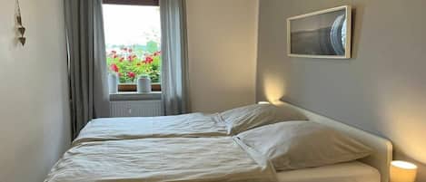 A bedroom with a bed, a window with curtains, a bedside lamp, and a framed picture on the wall.