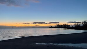 A coastal landscape with a calm body of water, a clear sky, and distant wind turbines.
