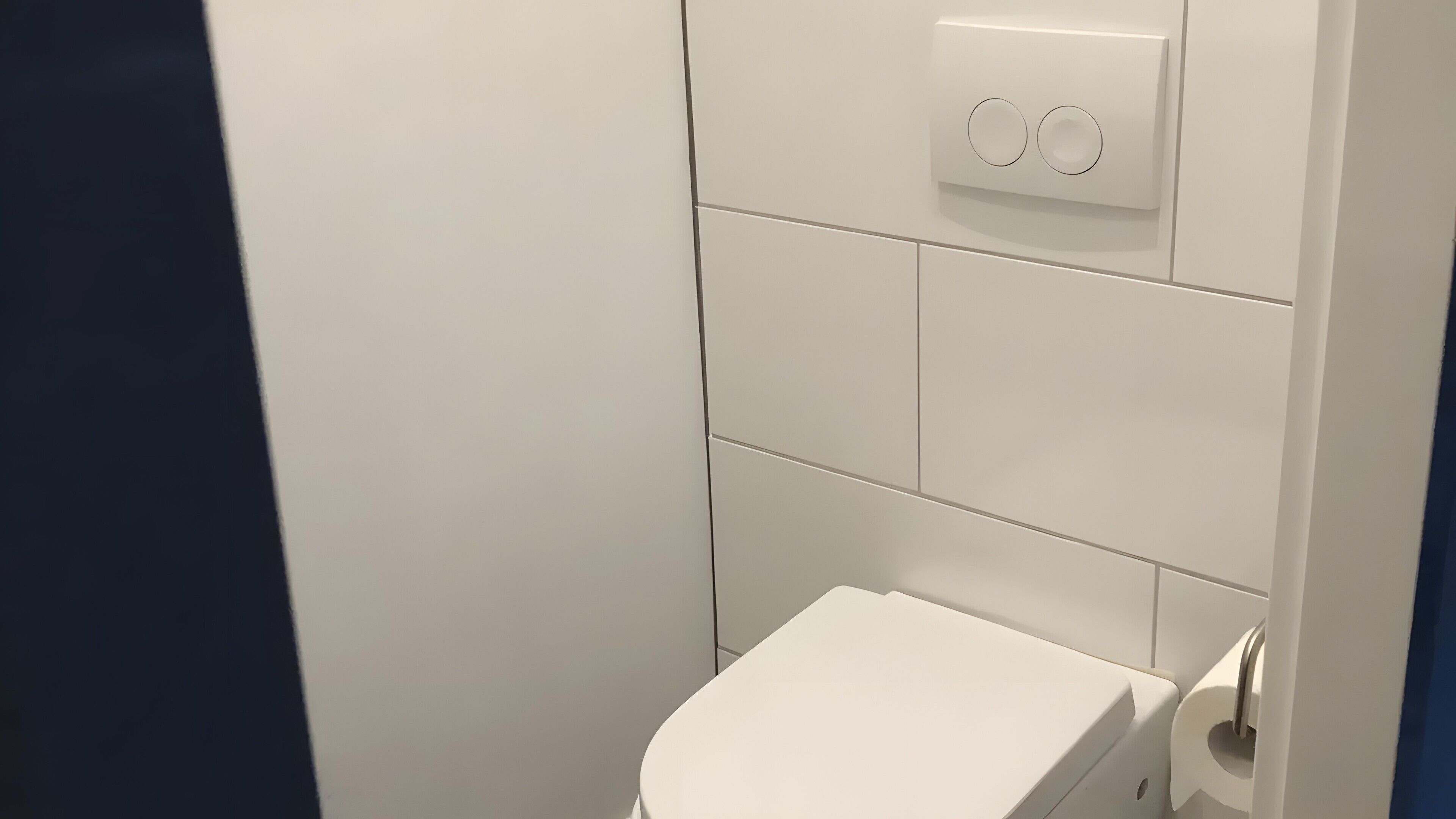 Inodoro blanco con palanca de descarga y pared blanca con interruptor de luz.
