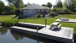 A house with a dock extending into a calm body of water, a grassy yard, and a small patio area with a table and benches. - Friesche Zusje Holiday Home with Terrace, Garden, Jetty & Wi-Fi in Makkum (Makkum)
