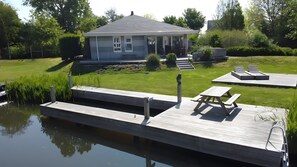 A house with a dock extending into a calm body of water, a grassy yard, and a small patio area with a table and benches. - Friesche Zusje Holiday Home with Terrace, Garden, Jetty & Wi-Fi in Makkum (Makkum)