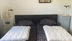 Ein Doppelbett mit schwarzem Kopfteil und weißer Bettwäsche, begleitet von Nachttischen mit Lampen und einem kleinen Schränkchen.