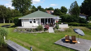 A house with a green roof, a porch with outdoor furniture, and a wooden deck with a bench. - Friesche Zusje Holiday Home with Terrace, Garden, Jetty & Wi-Fi in Makkum (Makkum)