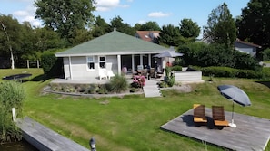 A house with a green roof, a porch with outdoor furniture, and a wooden deck with a bench. - Friesche Zusje Holiday Home with Terrace, Garden, Jetty & Wi-Fi in Makkum (Makkum)
