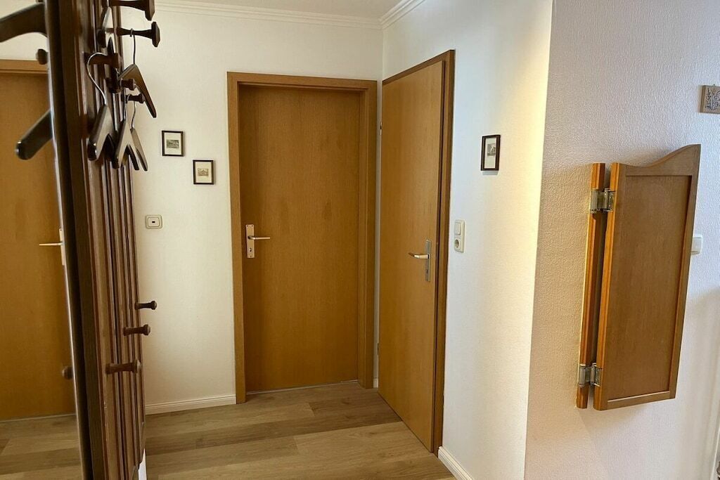 Un couloir avec des portes en bois, un porte-manteau et un meuble fixé au mur.