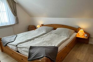 Een enkel bed met houten frame en twee nachtkastjes, elk met een lamp en een wekker.