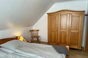 Ein Schlafzimmer mit einem Bett, einem Holzschrank, einem Stuhl und einem Nachttisch mit Lampe.