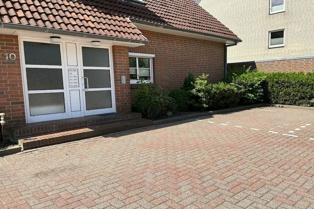 Edifício de tijolos com telhado de cerâmica, entrada numerada e acesso por calçada.