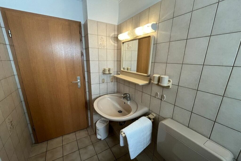 A bathroom with a wooden door, a sink, a mirror, and a bathtub.
