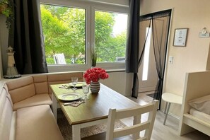 Een eethoek met een tafel gedekt voor twee personen, een bank en een raam met uitzicht op bomen.