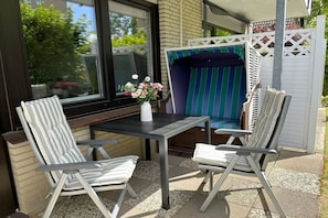An outdoor patio with two striped chairs, a table, and a small white vase with flowers. - Holiday apartment in Büsum with swimming pool (Büsum)