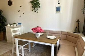 A dining area with a wooden table, white chairs, a cushioned bench, a vase with flowers, a framed picture, and wall decorations including a clock and butterflies. - Holiday apartment in Büsum with swimming pool (Büsum)