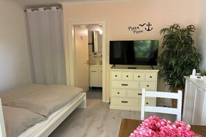 Een slaapkamer met een bed, een televisie, een dressoir, een stoel en een potplant.