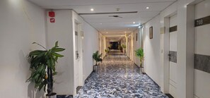 A hotel hallway with a marble floor, potted plants, and doors with room numbers. - Hotel Lee Grand Inn (Ahmedabad)