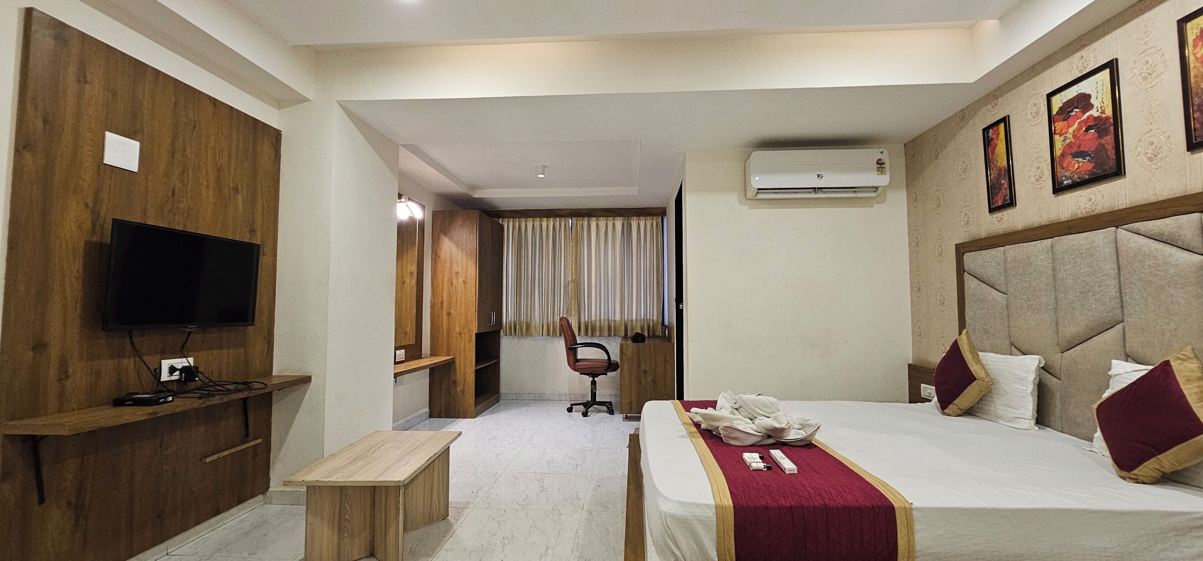 Habitación de hotel con cama, escritorio, silla, televisión y equipo de aire acondicionado.