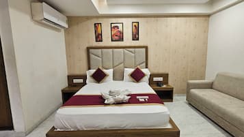 Habitación de hotel con una cama grande, cabecera, dos mesitas de noche, un sofá y una pared con tres cuadros enmarcados.