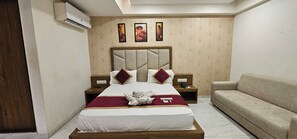 A hotel room with a large bed, a headboard, two nightstands, a sofa, and a wall with three framed pictures. - Hotel Lee Grand Inn (Ahmedabad)