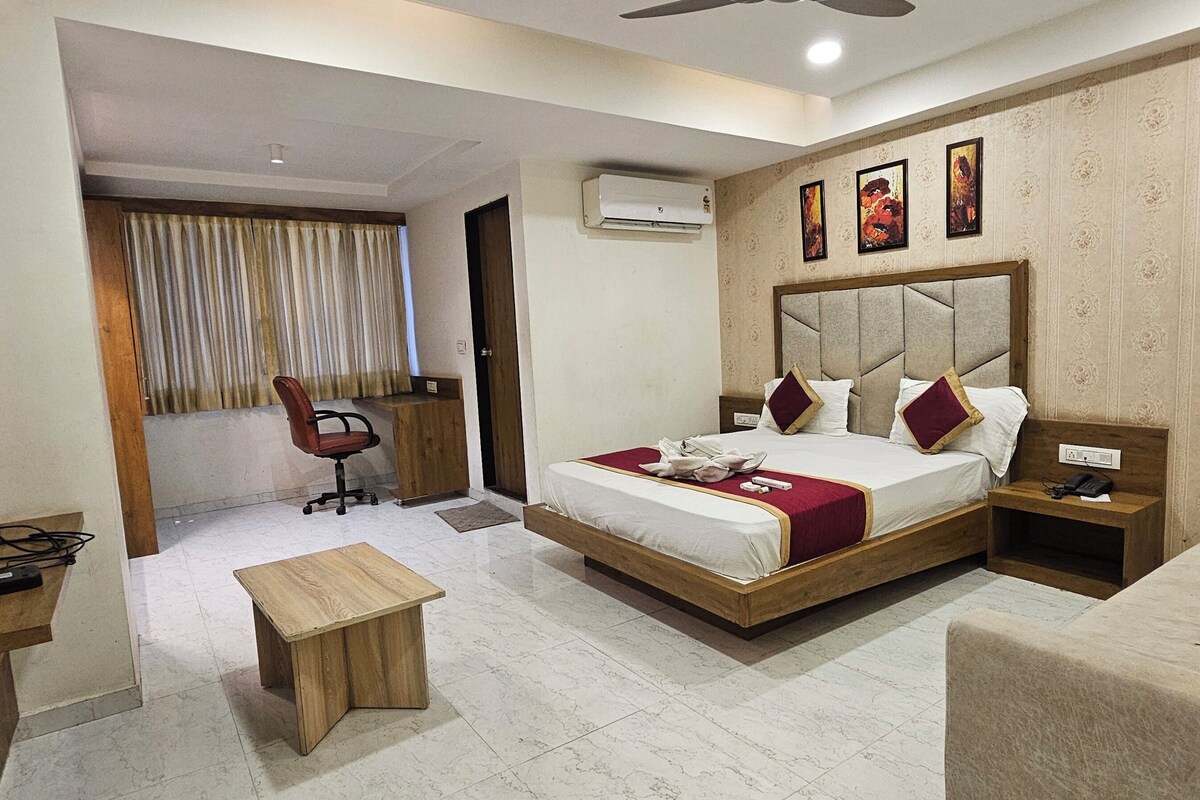A hotel room with a bed, a desk, a chair, a television, and an air conditioning unit.