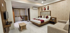 A hotel room with a bed, a desk, a chair, a television, and an air conditioning unit. - Hotel Lee Grand Inn (Ahmedabad)
