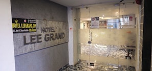 Entrada de un hotel con un letrero que dice HOTEL LEE GRAND, un número de contacto y una nota sobre disponibilidad de habitaciones con aire acondicionado en el séptimo piso.