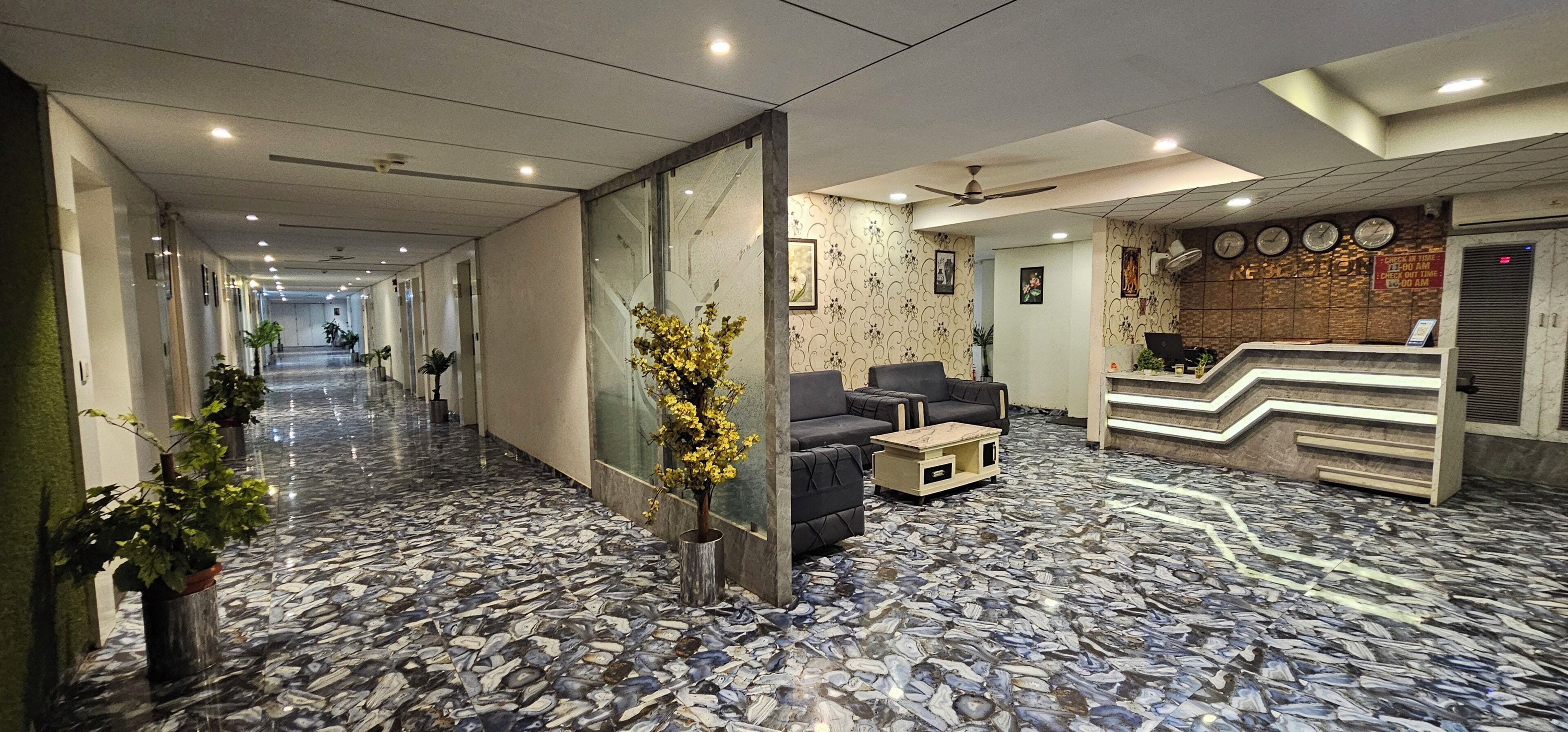 Un vestíbulo de hotel con suelo de mármol, zona de estar, mostrador de recepción y una escalera.