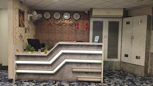 Un área de recepción con un letrero de check-in/out, relojes, un ordenador de escritorio y una fuente de agua.